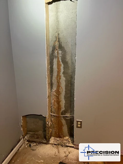Finished basement wall with drywall removed, showing a vertical foundation crack with orange-red clay and water stains running down the concrete to the floor